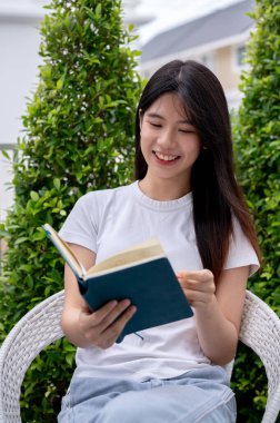 Mutlu, çekici Asyalı bir kadın aydınlık bir günde evinin bahçesinde kitap okumaktan zevk alıyor. Boş zaman, boş zaman, hobi, yaşam tarzı