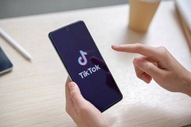 Chiang Mai, Tayland - Haziran 03 2024: Kapalı bir masadaki ekranda TikTok logosu olan akıllı telefonu tutan bir kadının yakın plan görüntüsü. Sosyal medya platformu kavramı