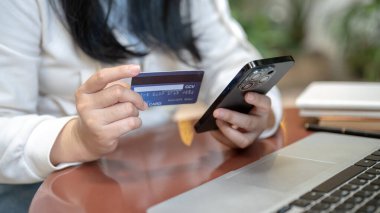 Parasını transfer etmek için mobil bankacılık uygulamasını kullanan, akıllı telefonu ve kredi kartını açık bir masada tutan Asyalı bir kadının kırpılmış görüntüsü. insanlar ve finansal kavramlar