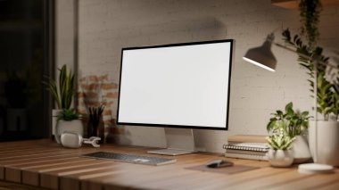 Beyaz ekranlı bir bilgisayar ahşap bir masanın üzerinde beyaz tuğla bir duvara karşı, karanlık bir odada, loş bir lambanın ışığıyla aydınlatılıyor. 3d görüntüleme, 3d illüstrasyon