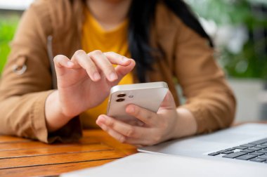 Bir kafede uzaktan çalışırken akıllı telefonunu kullanan Asyalı bir kadının kırpılmış görüntüsü. sohbet etmek, mesajları cevaplamak, uygulamayı, insanları ve kablosuz teknoloji kavramlarını kaydırmak