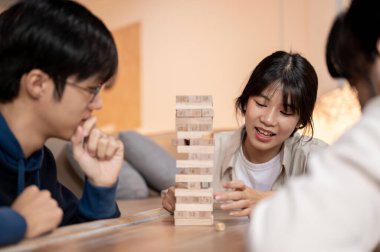 Genç mutlu Asyalı arkadaşlar evde Jenga ya da tahta bloklar oynamaktan zevk alıyorlar, masa oyunu oynayarak eğleniyorlar. Boş zaman, aktivite, eğlence