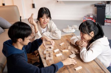 Bir grup neşeli Asyalı genç arkadaş oturma odasında masa oyunu oynuyorlar, tahta blok oyunu ya da Jenga oynuyorlar, evde eğlenceli bir parti veriyorlar. eğlence ve dostluk kavramları