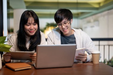 İki genç Asyalı üniversite öğrencisi ödev yapıyor, bir kafede ortak bir proje üzerinde çalışıyorlar, fikirleri tartışıyorlar, ve bir dizüstü bilgisayara bakıyorlar..