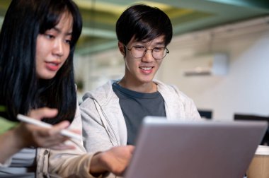 İki genç Asyalı üniversite öğrencisi ödev yapıyor, bir kafede ortak bir proje üzerinde çalışıyorlar, fikirleri tartışıyorlar, ve bir dizüstü bilgisayara bakıyorlar..