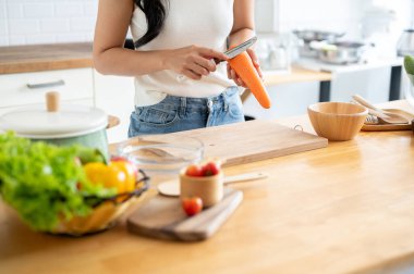 Kopya alanı olan kesilmiş bir resim bıçakla havuç soyan bir kadın mutfaktaki mutfak masasında yemek pişiren bir kadın. Ev yemeği, sağlıklı yaşam tarzı, sağlıklı beslenme, kilo verme tarifleri.