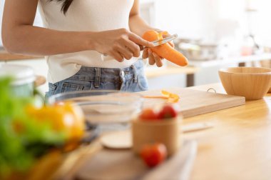Kopya alanı olan kesilmiş bir resim bıçakla havuç soyan bir kadın mutfaktaki mutfak masasında yemek pişiren bir kadın. Ev yemeği, sağlıklı yaşam tarzı, sağlıklı beslenme, kilo verme tarifleri.
