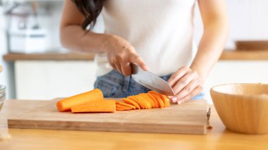 Ahşap mutfak masasında havuç doğrayan, mutfakta yemek pişiren bir kadının yakın plan görüntüsü. sağlıklı yiyecekler, yaşam tarzı, ev yemekleri