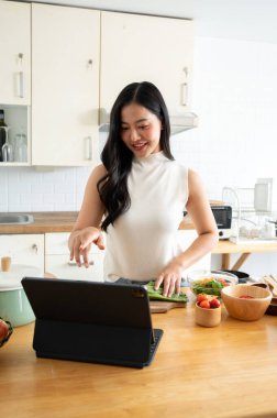 İnternette yemek pişirirken dijital tabletini kullanan genç ve güzel bir Asyalı kadın. ev yemeği ve yaşam tarzı kavramları
