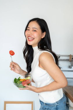Çekici, gülümseyen Asyalı bir kadın kameraya gülümsüyor, elinde sağlıklı bir salata kasesi, mutfakta duruyor. Ev yemekleri, sağlıklı yaşam tarzı, sağlıklı yaşam.
