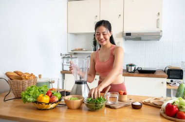 Güzel, sağlıklı, spor giyimli Asyalı bir kadın mutfakta sağlıklı smoothie içeceğini hazırlıyor, blender kullanarak, blender 'a biraz sebze ekliyor. sağlıklı yiyecekler, diyet, sağlık yaşam tarzı