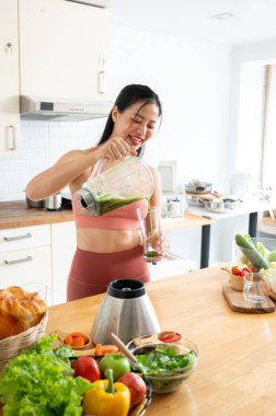 Çekici, sağlıklı bir Asyalı kadın spor giyim sektöründe yeşil suyunu blenderdan dolduruyor, evde yaptığı çalışmadan sonra ona sağlıklı bir içecek hazırlıyor. sağlıklı yaşam tarzı, ev hayatı, sağlıklı yaşam.