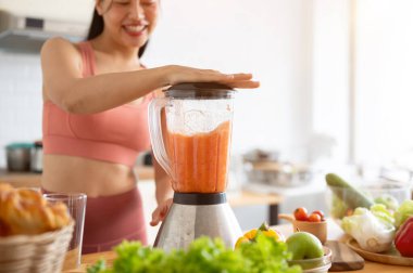 Sağlıklı, formda, spor kıyafetli bir Asyalı kadının blender ile mutfakta smoothie yaparken çekilmiş bir görüntüsü. sağlıklı yaşam tarzı, refah, ev hayatı, seçici odaklanma imajı