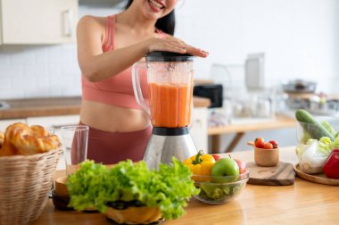 Sağlıklı, formda, spor kıyafetli bir Asyalı kadının blender ile mutfakta smoothie yaparken çekilmiş bir görüntüsü. sağlıklı yaşam tarzı, refah, ev hayatı, seçici odaklanma imajı