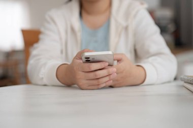 Kapüşonlu bir kadının kesilmiş bir görüntüsü bir kafede oturuyor ve akıllı telefonunu kullanıyor, telefonunu kaydırıyor, mobil bir uygulama kullanıyor, sosyal medyada sohbet ediyor. İnsanlar, yaşam tarzı, kablosuz teknoloji