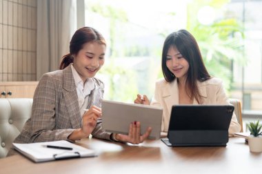 İki genç, pozitif Asyalı iş kadını dijital tabletleri üzerinde çalışıyorlar, gayri resmi bir toplantı yapıyorlar ve bir kafede birlikte çalışıyorlar..