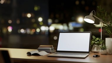 A close-up image of a laptop computer with a white-screen mockup and accessories on wooden table against the window with city nightlight view. office at night concept, 3d render, 3d illustration clipart