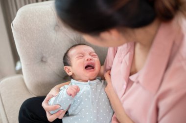 Sevimli bir erkek bebek annesinin kollarında ağlıyor, rahatsız ya da aç hissediyor. Çocukluk, süt, emzirme.