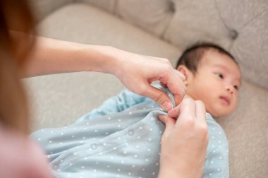 Şefkatli bir anne, yeni doğmuş bebeğinin üzerine pijama koyuyor oturma odasındaki bir kanepede. Kopyalama alanı olan yakın plan bir resim. annelik ve çocuk bakımı kavramları