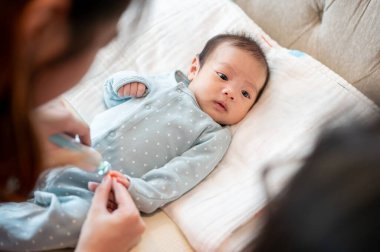Pijamalı sevimli bir erkek bebek yatağında ve tırnaklarını annesi tarafından tutulan elektronik bir bebek tırnak makasıyla kestiriyor. çocuk bakımı kavramı