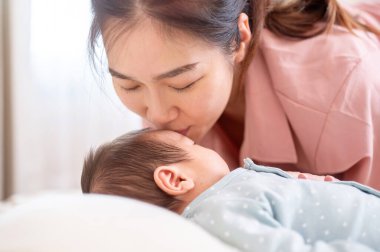 Asyalı bir annenin, yeni doğmuş bebeğinin uyurken alnını öptüğü yakın plan bir görüntü. Annelik, sevgi ve şefkat.,
