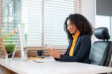 Başarılı, pozitif iş kadını takım elbiseli bir iş kadını ofisteki masasında akıllı telefonunu kullanıyor. telefonda kaydediliyor, mesajları kontrol ediyor, sohbete cevap veriyor