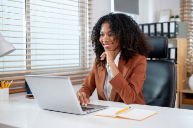 Takım elbiseli çekici, profesyonel bir siyahi iş kadını özel ofisinde bilgisayarının başında çalışıyor..