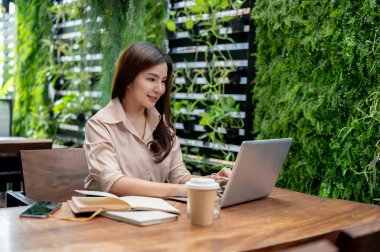 Güzel, kendine güvenen Asyalı bir kadın bir kafede çalışıyor, dizüstü bilgisayarı üzerinde çalışıyor. Serbest çalışan, iş kadını, üniversite öğrencisi.