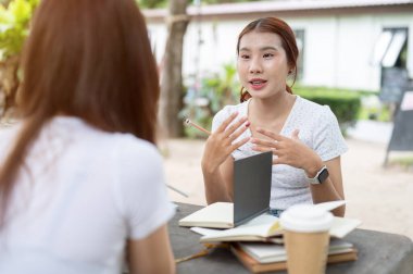 Olumlu, arkadaş canlısı genç Asyalı bir üniversite öğrencisi arkadaşıyla parkta bir masada ödev yapıyor, konuşuyor, tartışıyor, matematik ödevinde arkadaşına yardım ediyor..