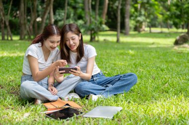 İki sevimli genç Asyalı bayan arkadaş parkta çimenlerde dinlenirken akıllı telefondan konuşmaktan ve bir şeyler izlemekten zevk alıyorlar. Arkadaşlık, yaşam tarzları, kablosuz teknoloji