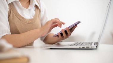 Bir kadının, en az beyaz bir odada, masasında akıllı telefonunu kullanırken, bir kafede uzaktan çalışırken, akıllı telefonundan mesajları kontrol ederken, birden fazla iş yaparken yakın plan görüntüsü..
