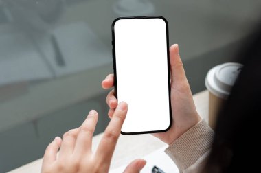 Kapalı alanda otururken akıllı telefonunu kullanan Asyalı bir kadının ekrana dokunuşunun yakın plan görüntüsü. Beyaz ekran maketi olan bir akıllı telefon. İnsanlar ve kablosuz teknoloji