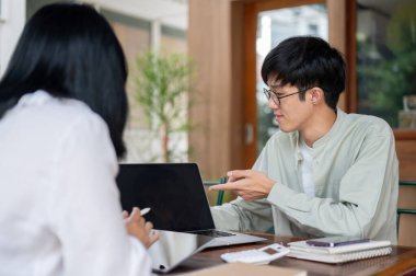 Zeki bir Asyalı genç adam, bir kafede meslektaşı ile iş birliği yapmak için toplantı yapıyor. Parmağını bir dizüstü bilgisayarı işaret ediyor ve fikirlerini anlatıyor..