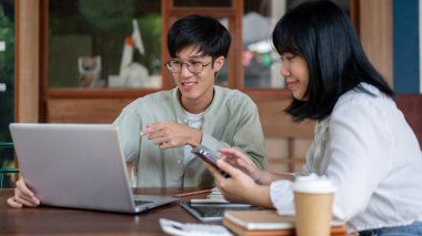 Zeki bir Asyalı genç adam, bir kafede meslektaşı ile iş birliği yapmak için toplantı yapıyor. Parmağını bir dizüstü bilgisayarı işaret ediyor ve fikirlerini anlatıyor..