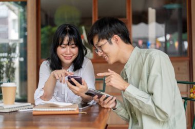 İki mutlu Asyalı genç arkadaş, şehirde bir kafede oturup akıllı telefondan video izlerken konuşmaktan zevk alıyorlar. İnsanlar, yaşam tarzı ve kablosuz teknoloji
