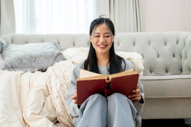 Güzel, mutlu bir Asyalı kadın oturma odasında kitap okuyup evde ders çalışmaktan zevk alıyor. Boş zaman, hobi, ev hayatı.