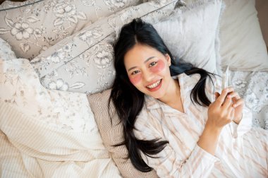 Güzel, mutlu, pijamalı, yüzünde bantlarla yatakta kameraya gülümseyen bir Asyalı kadın resmi. insanlar ve ev hayatı kavramları