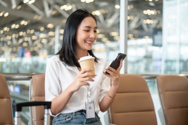 Güzel bir Asyalı iş kadını havaalanı terminalinde bekleme koltuğunda oturmuş yatma zamanını beklerken akıllı telefonunu kullanıyor. insanlar ve ulaşım kavramları