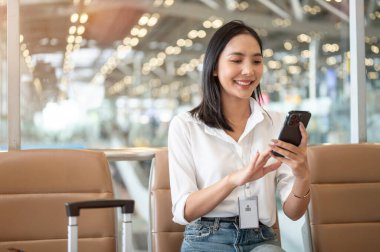 Güzel bir Asyalı iş kadını havaalanı terminalinde bekleme koltuğunda oturmuş yatma zamanını beklerken akıllı telefonunu kullanıyor. insanlar ve ulaşım kavramları