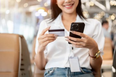 Havaalanı terminalinde otururken elinde kredi kartı ve akıllı telefon tutan güzel bir Asyalı kadının kesilmiş görüntüsü. insanlar, yaşam tarzı, finansal