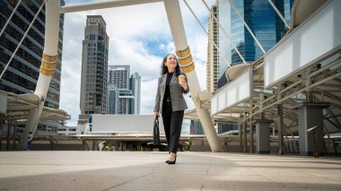 Kendine güvenen, mutlu, takım elbiseli Asyalı bir iş kadını sabah işe gidip geliyor. Etrafı gökdelen binalarıyla çevrili. Kopyalama alanı olan tüm gövde resmi