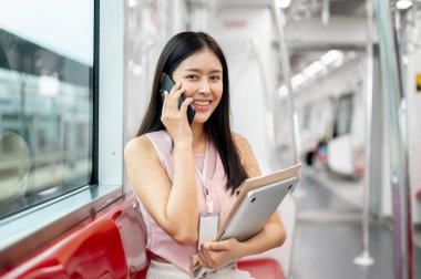 Güzel, pozitif Asyalı bir işkadını ya da ofis çalışanı sabah işe giderken biriyle telefonda konuşuyor, modern bir şehirde toplu taşıma araçlarıyla gidip geliyor..