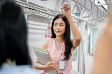 Olumlu bir Asyalı genç iş kadını işe gitmek için bir gökyüzü trenine biniyor, bir tırabzan tutuyor, kalabalık bir şehirde toplu taşıma araçlarıyla gidip geliyor. insanlar ve ulaşım kavramları