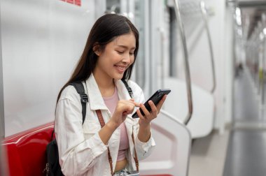 Çekici, mutlu, Asyalı genç bir bayan turist telefonda konuşuyor ya da bir gökyüzü treninde ya da metro istasyonunda otururken telefonunu kullanıyor, toplu taşıma araçlarıyla şehir merkezine gidip geliyor..