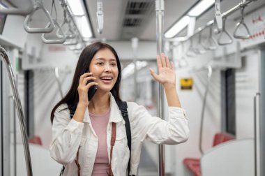 Neşeli, çekici Asyalı genç bir bayan turist telefonda konuşuyor ve el sallıyor. Şehir merkezinde ya da yeraltında trenle gidip gelirken birini selamlıyor..