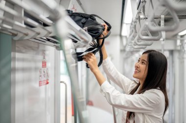Mutlu, çekici, genç Asyalı bir bayan yolcu sırt çantasını bir gökyüzü treninde ya da bir şehirde metro treninde giderken üstteki bagaj boşluğuna koyuyor. toplu taşıma kavramı