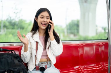 Güzel, mutlu, Asyalı genç bir bayan yolcu, bir gökyüzü treninde otururken telefonda konuşuyor, toplu taşıma araçlarıyla gidip geliyor..