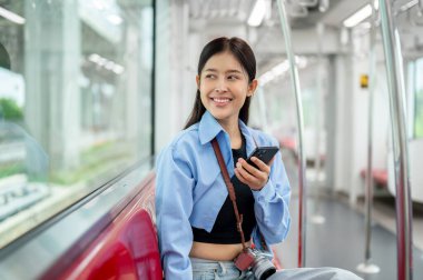 Güzel, genç, Asyalı bir bayan yolcu elinde akıllı bir telefonla gökyüzü treninde oturuyor, dışarıdaki manzaraya bakıyor, toplu taşıma araçlarıyla gidip geliyor..