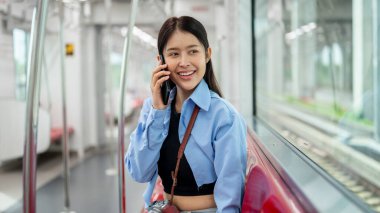 Güzel, mutlu Asyalı genç bir bayan yolcu, bir gökyüzü treninde otururken telefonla konuşuyor, toplu taşıma ile gidip geliyor, dışarıdaki manzaraya bakıyor..
