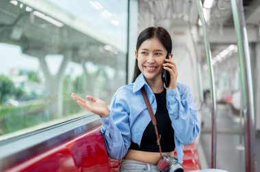 Güzel, mutlu Asyalı genç bir bayan yolcu, bir gökyüzü treninde otururken telefonla konuşuyor, toplu taşıma ile gidip geliyor, dışarıdaki manzaraya bakıyor..